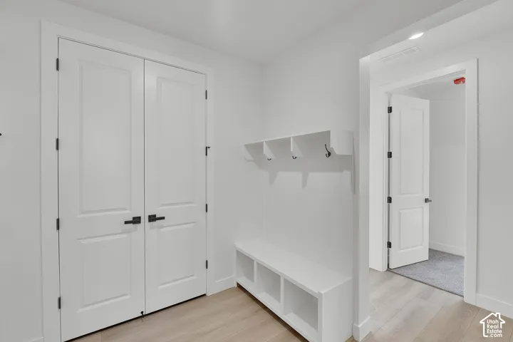 Built-in bench with integrated shelving and wall-mounted hooks, white paneled doors with matte black hardware, and wood-finish flooring