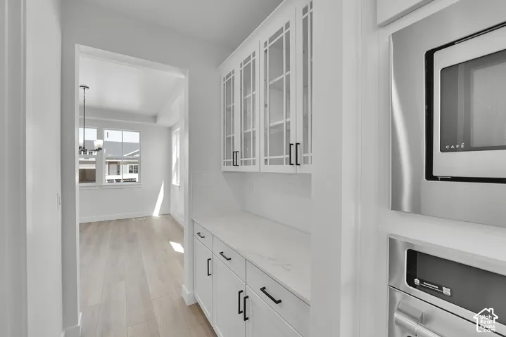 Built-in white cabinetry with glass-front uppers, stainless steel microwave, and wood-finish flooring