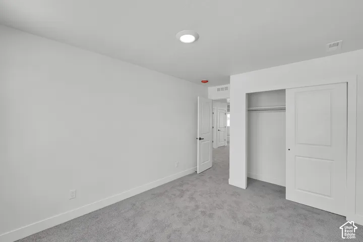 White painted walls, gray carpet, recessed ceiling light, white sliding closet doors, and a white interior door with dark hardware