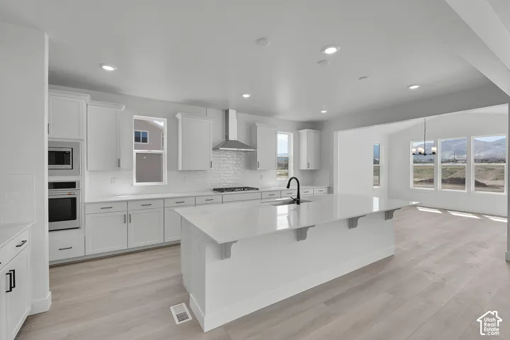 Open-concept kitchen featuring an expansive island with seating, a stainless steel range hood, built-in microwave and oven, recessed lighting, and wood-finish flooring