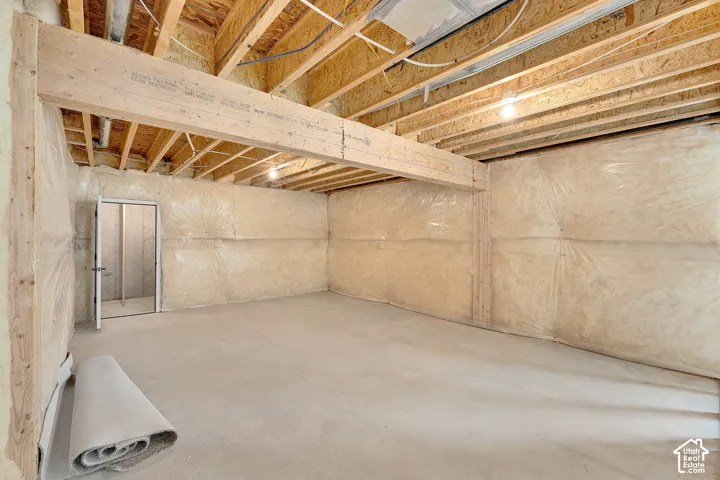 Unfinished basement featuring exposed wood joists, concrete flooring, insulated perimeter walls, and a utility door