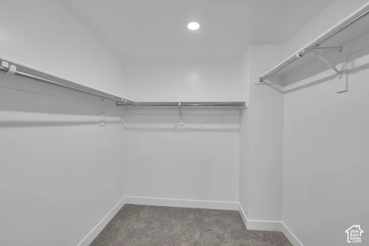 Walk-in closet with ample shelving, multiple chrome hanging rods, recessed lighting, and grey carpeting