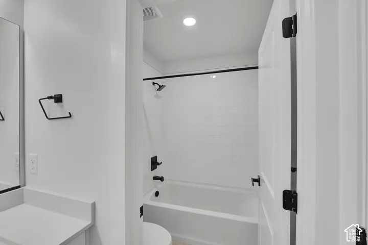 Tub and shower combination with subway tile surround, matte black fixtures, and a white finish vanity with a light countertop