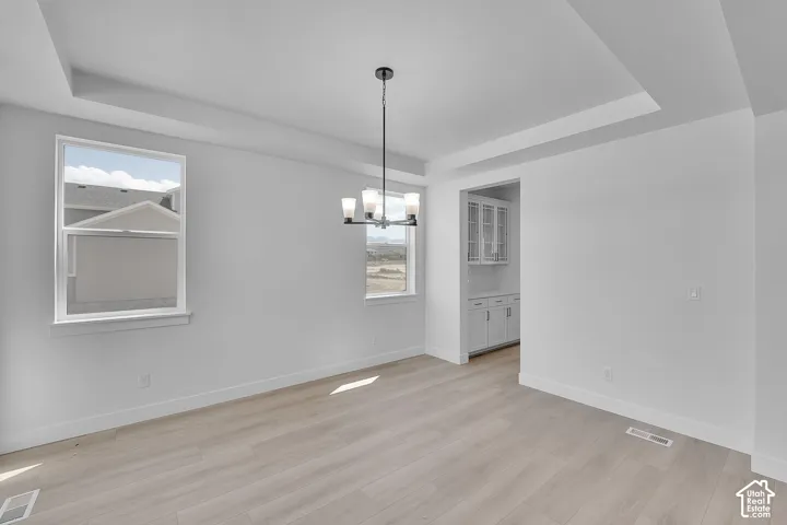 Tray ceiling with an attached chandelier, wood-finish flooring, and white walls