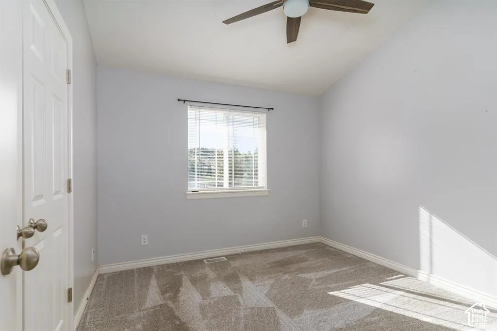 Sloped ceiling featuring a ceiling fan, neutral tone wall paint, carpeted flooring, and a large window