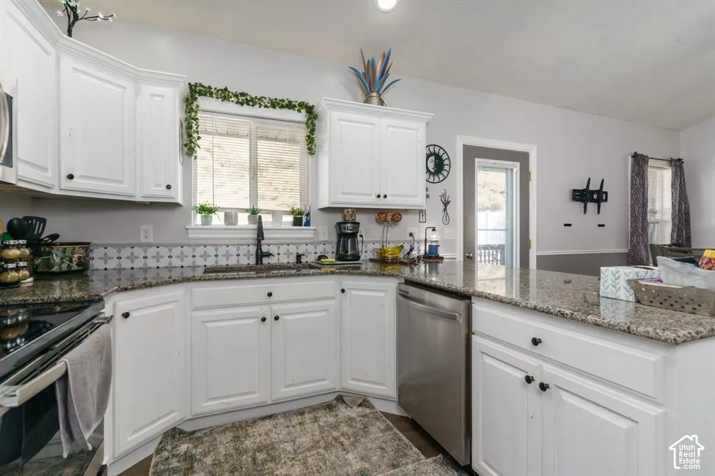 White cabinetry, granite countertops, stainless steel dishwasher, patterned tile backsplash, and a black gooseneck faucet