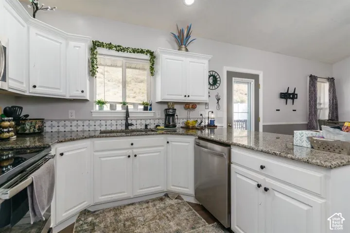 White cabinetry, granite countertops, stainless steel dishwasher, patterned tile backsplash, and a black gooseneck faucet