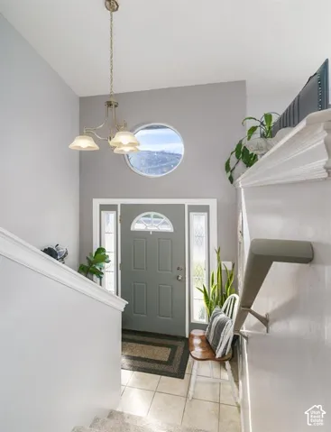Entryway featuring a decorative round window, a three-light chandelier, a paneled door with sidelights, and light-toned tile flooring