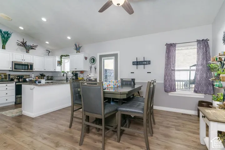 Vaulted ceiling with recessed lighting, white cabinetry, stainless steel appliances, kitchen island with granite-style countertop, and wood-finish flooring