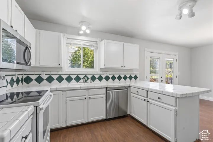 White paneled cabinetry, stainless steel appliances, tile countertops, and wood-finish flooring