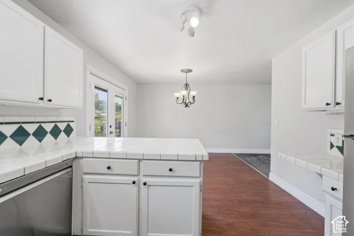 White cabinetry with contrasting dark hardware, tile countertops, and a decorative tile backsplash