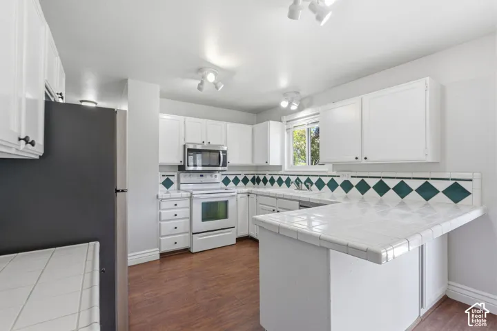 White cabinetry with dark hardware, tile countertops, integrated stainless steel microwave, white range, and wood-finish flooring
