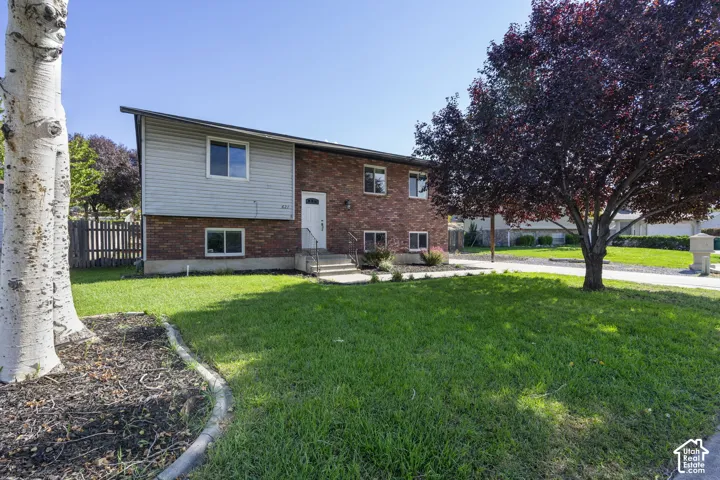 Brick and siding exterior, concrete walkway, mature tree, fenced yard, and front lawn