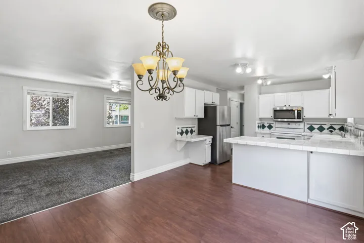 Hardwood-finish flooring, white cabinetry, stainless steel appliances, white tile countertops, and recessed lighting