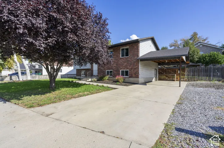 Brick and siding exterior with a covered carport, concrete driveway, and mature landscaping