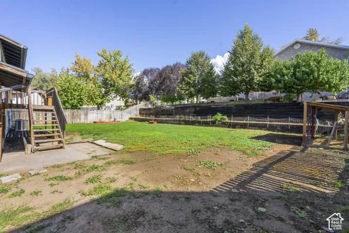Expansive backyard featuring a tiered retaining wall, wood fencing, and a concrete patio with wood stairs