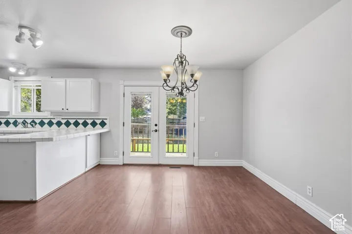 Wood-finish flooring, white cabinetry, ceramic tile backsplash, track lighting, and a decorative chandelier with a ceiling medallion