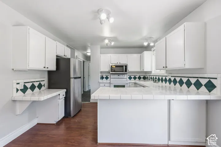 White cabinetry with dark hardware, white tile countertops, patterned tile backsplash, stainless steel refrigerator, and wood-finish flooring