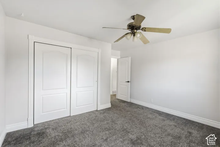 Neutral wall paint with textured carpeting, dual panel closet doors, and an overhead ceiling fan with lighting