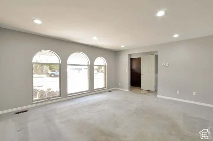Triple arched windows, recessed ceiling lighting, light gray wall paint, and gray carpet flooring