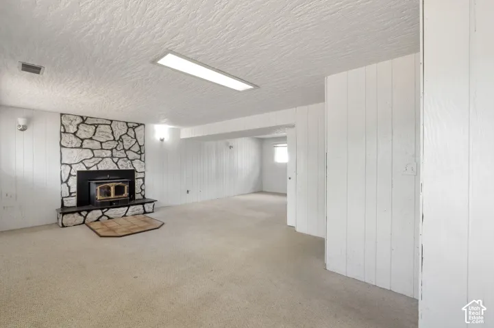 Spacious room featuring a stone-faced fireplace with an insert, carpeted flooring, and white paneled walls