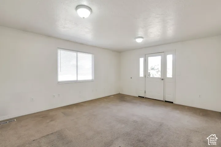Entry door with two sidelight windows, flush-mount ceiling lights, and a window with blinds