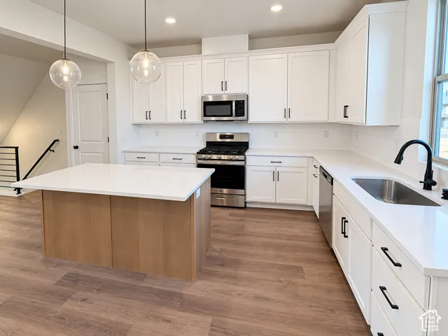 White shaker cabinetry, stainless steel appliances, white subway tile backsplash, wood-finish flooring, and a central island with a white countertop