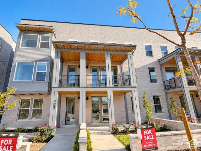 Brick exterior with contrasting siding accents, multiple balconies with metal railings, light-colored entry doors, concrete pathways, and built-in planters with landscaping