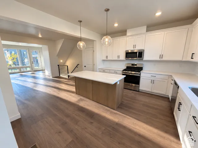 Contemporary kitchen with white shaker cabinetry, stainless steel appliances, a center island with a light wood finish, and wood-finish flooring