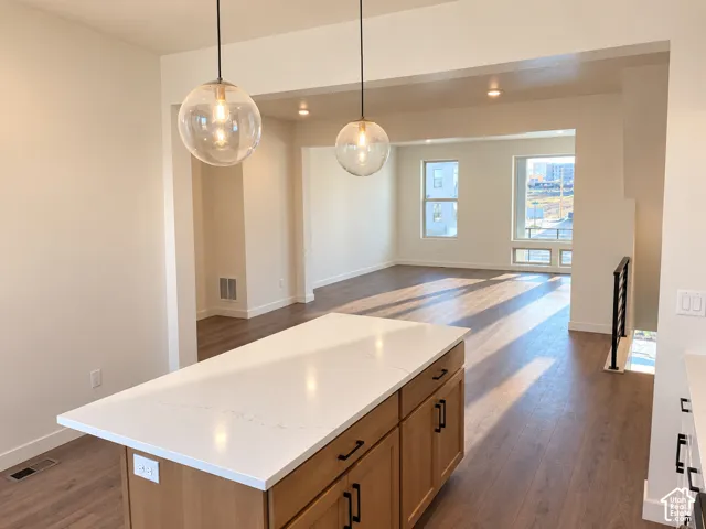 Kitchen island with white countertop, wood-finish cabinetry, and contemporary pendant lighting