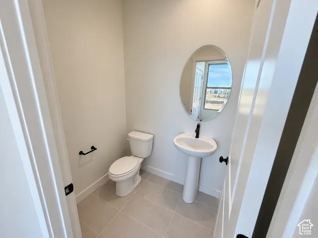 Neutral-toned tile flooring, pedestal sink with matte black faucet, oval mirror, and a white commode