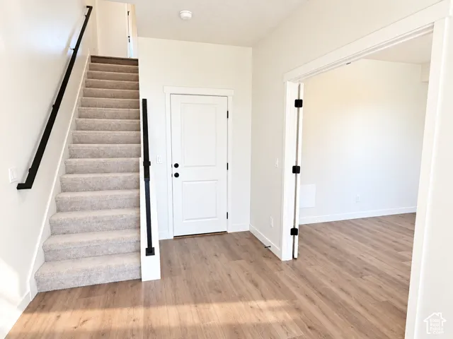 Wood-finish flooring, white walls, and a carpeted staircase with a black metal handrail