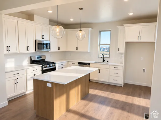 White shaker cabinetry, light wood-finish flooring, central island with solid surface countertop, stainless steel appliances, and two pendant light fixtures