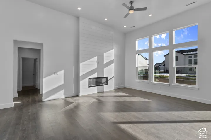 Spacious room with high ceilings, wood-finish flooring, a modern linear fireplace, and multiple tall windows