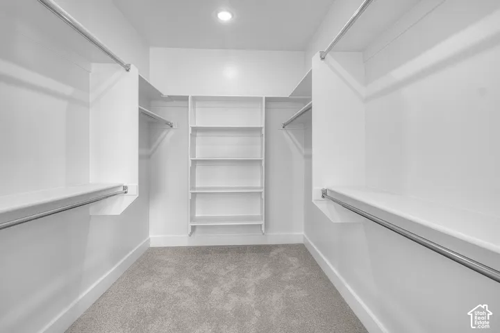 Walk-in closet with integrated shelving, multiple hanging rods, and recessed lighting over carpet flooring