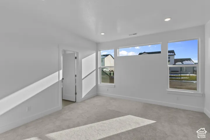 Neutral-toned carpeting, white walls, multiple windows, recessed lighting, and a white interior door
