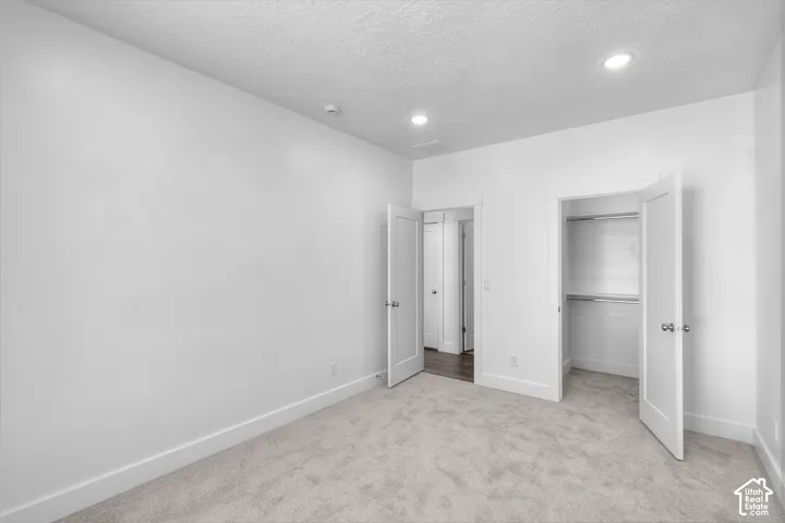 Recessed lighting, light-toned carpeting, white interior doors, and a built-in closet with shelving and hanging rods