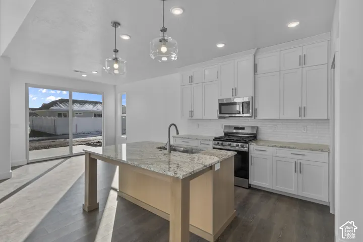 Kitchen featuring white cabinetry, light-toned granite countertops, stainless steel appliances, and a subway tile backsplash