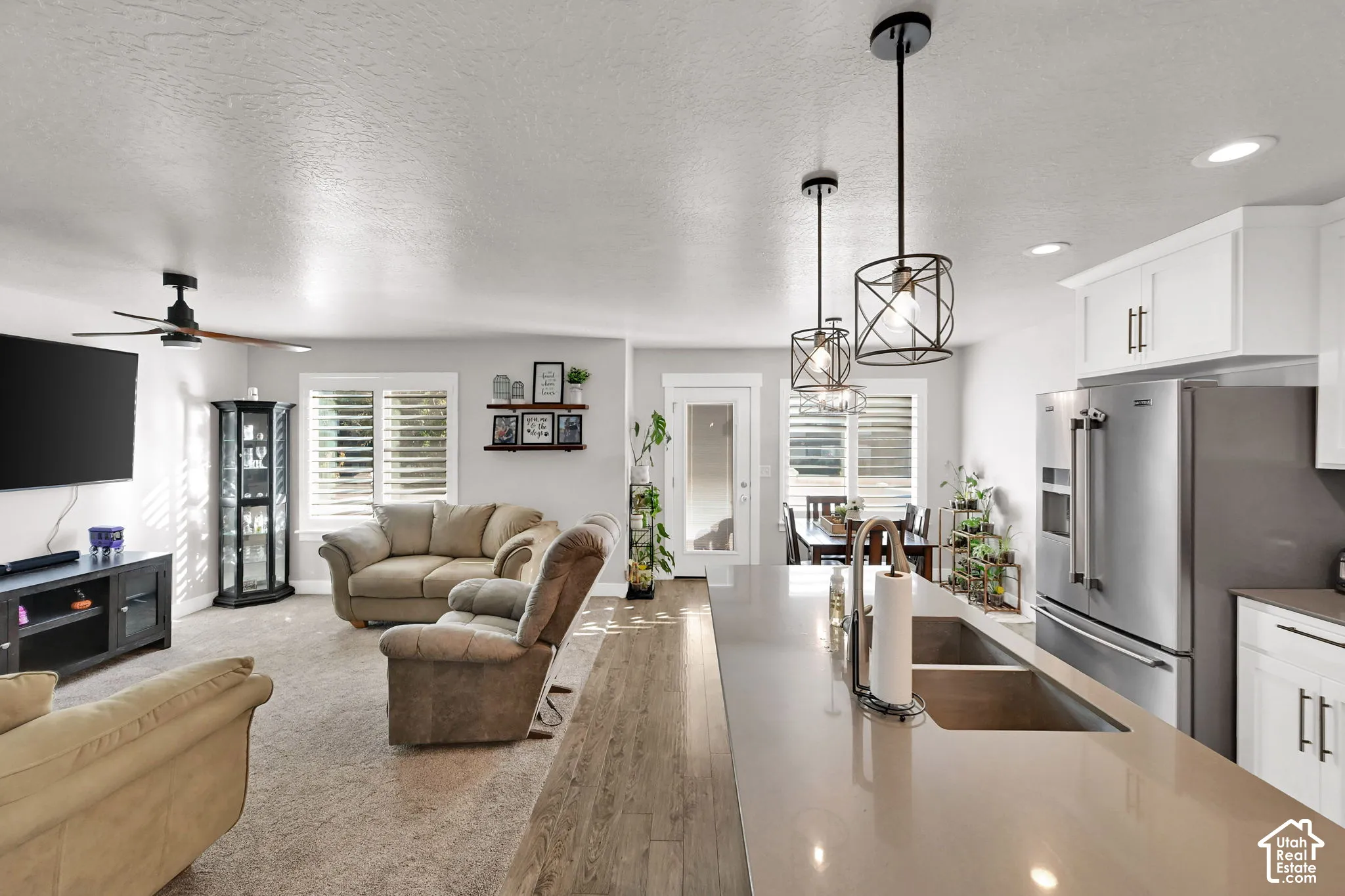 Spacious interior featuring a kitchen island with dual sinks, stainless steel appliances, white cabinetry, and wood-finish flooring