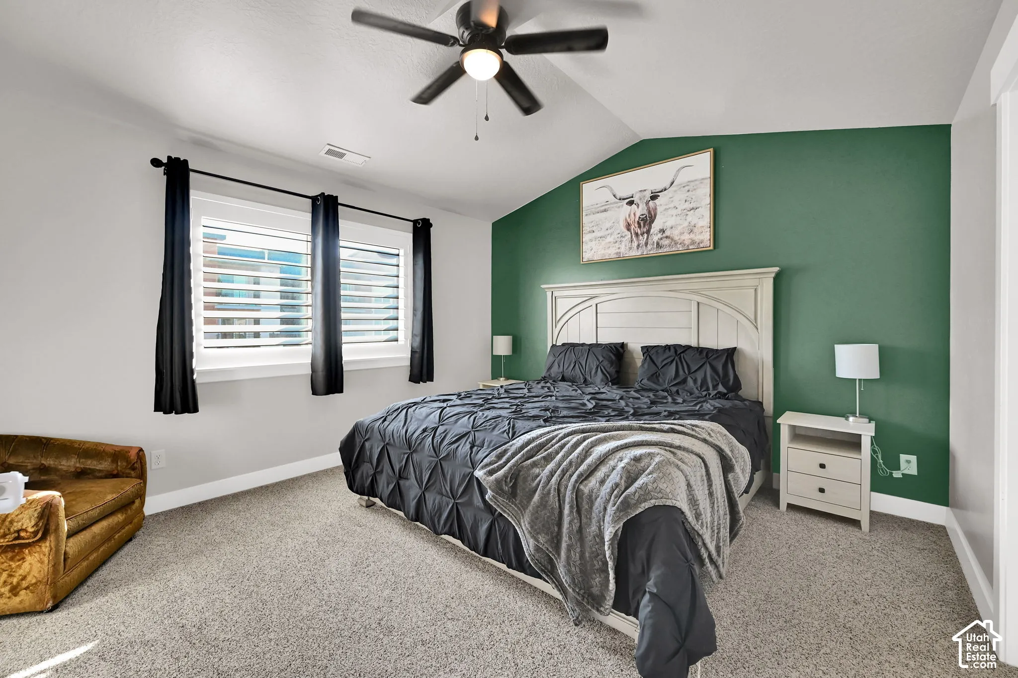 Vaulted ceiling, ceiling fan, twin windows with plantation shutters, accent wall, and neutral carpet flooring
