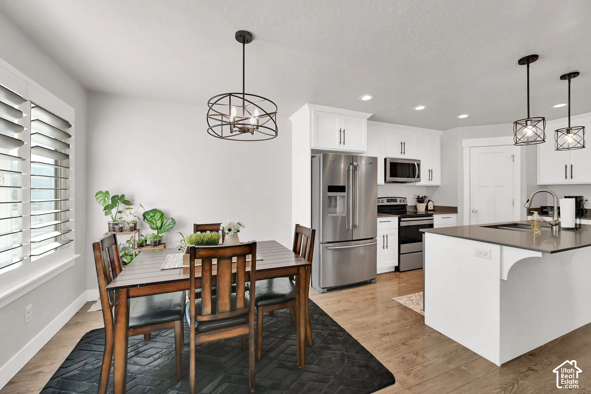 Wood-finish flooring, white cabinetry, stainless steel appliances, and a kitchen island with sink