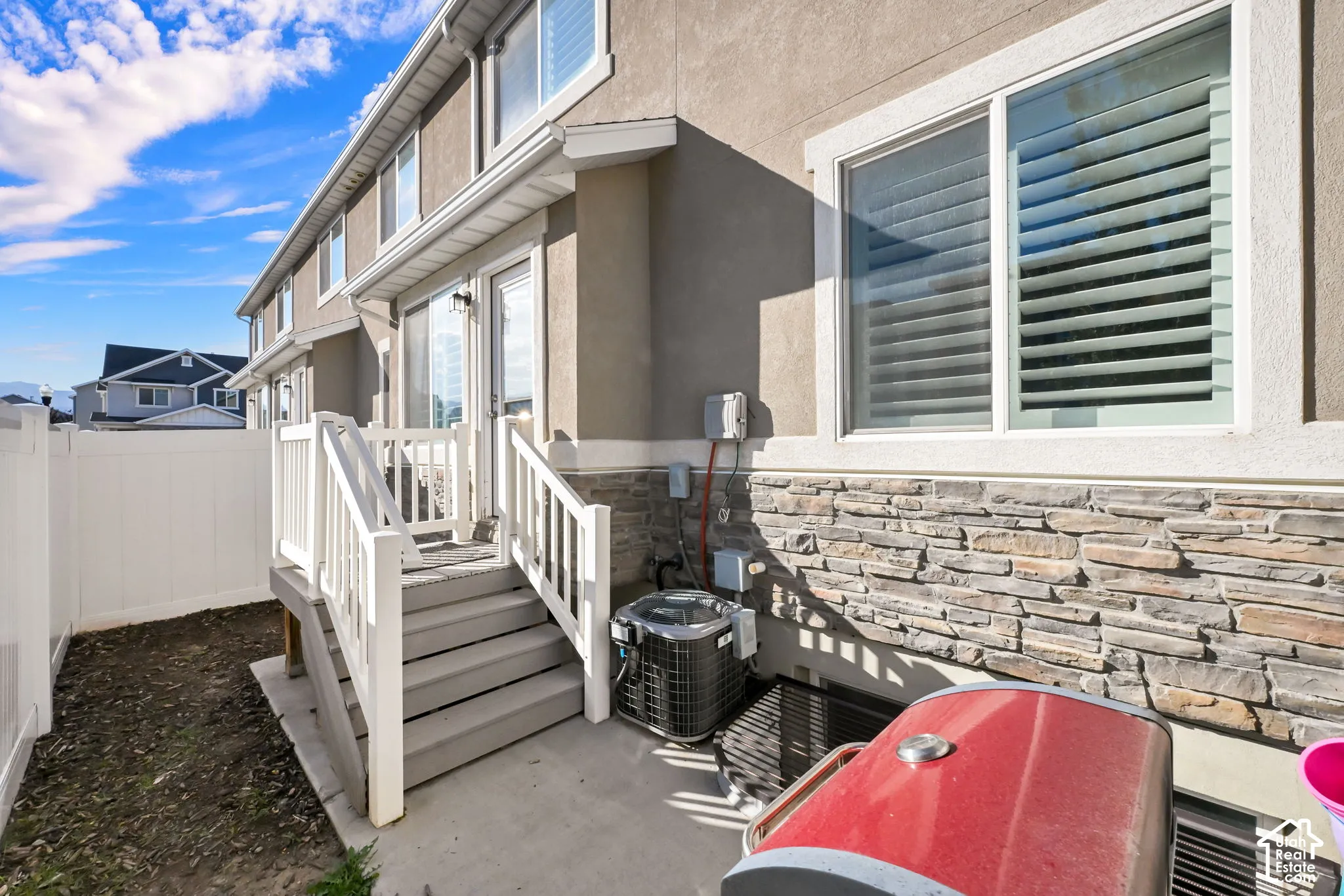 Rear exterior featuring a multi-level deck, white railing, privacy fencing, and stone veneer accents