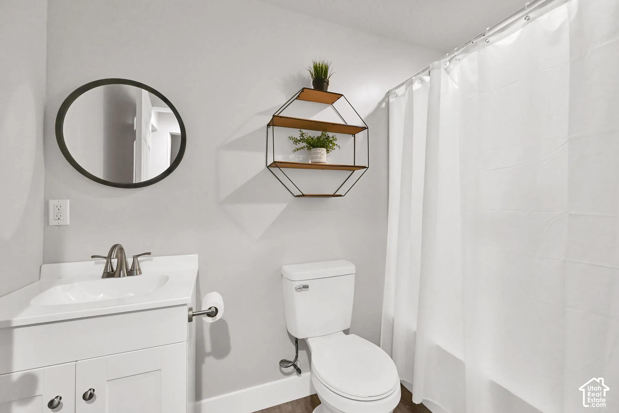 White vanity with integrated sink, brushed nickel faucet, wall-mounted mirror, white toilet, and enclosed shower