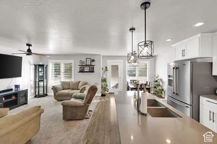 Spacious interior featuring a kitchen island with dual sinks, stainless steel appliances, white cabinetry, and wood-finish flooring