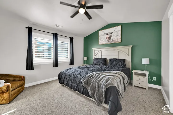 Vaulted ceiling, ceiling fan, twin windows with plantation shutters, accent wall, and neutral carpet flooring