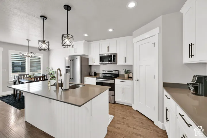 Modern kitchen featuring an expansive center island, stainless steel appliances, contemporary pendant lighting, recessed ceiling lighting, and white cabinetry