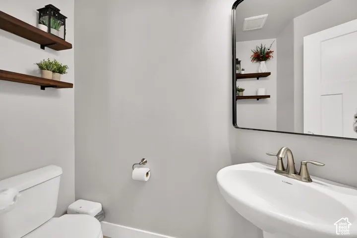 Pedestal sink with brushed metal faucet, rectangular framed mirror, and two wall-mounted wood-finish shelves