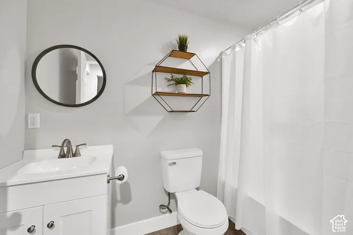 White vanity with integrated sink, brushed nickel faucet, wall-mounted mirror, white toilet, and enclosed shower