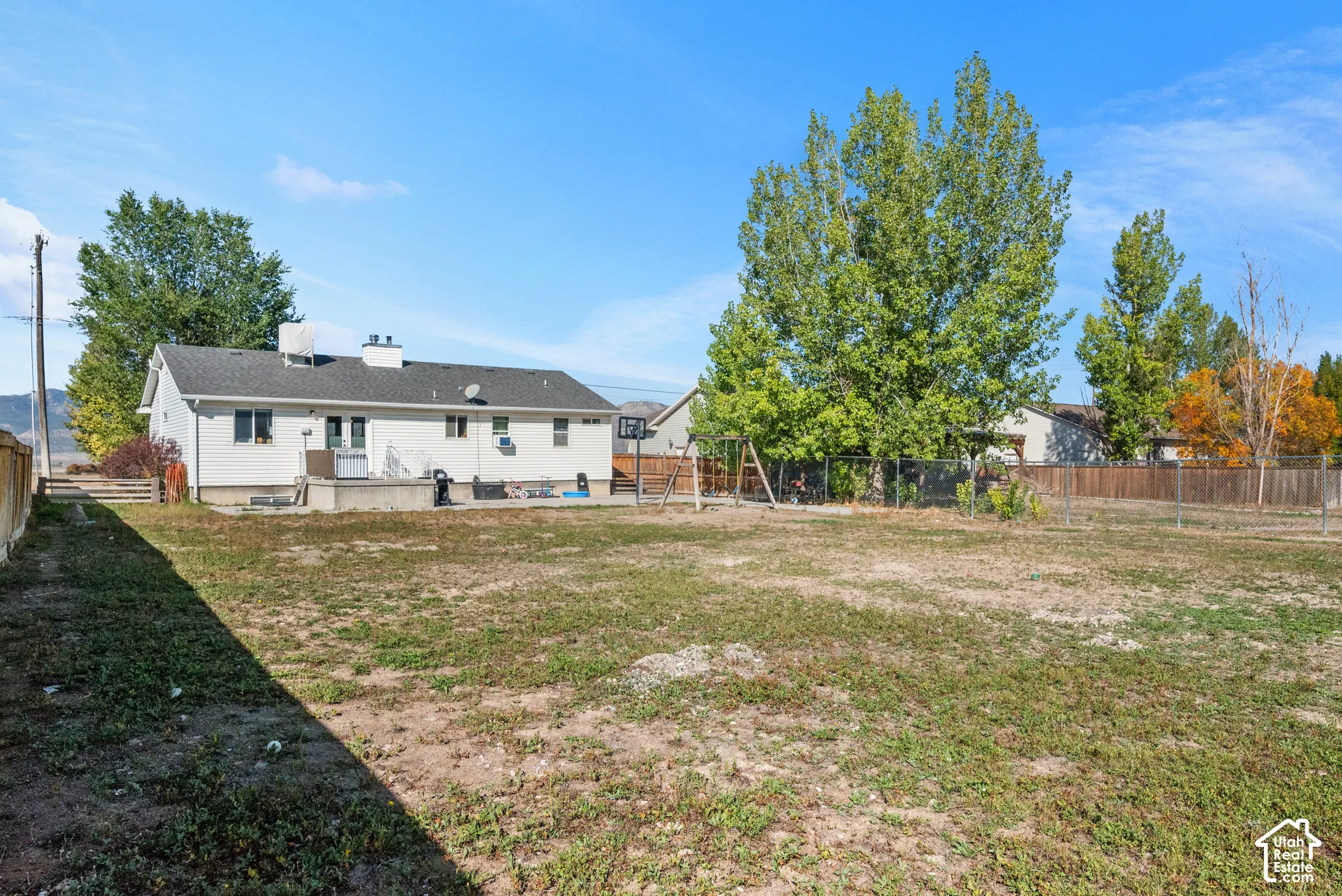 Expansive backyard featuring a large green space, mature trees, and a wooden privacy fence