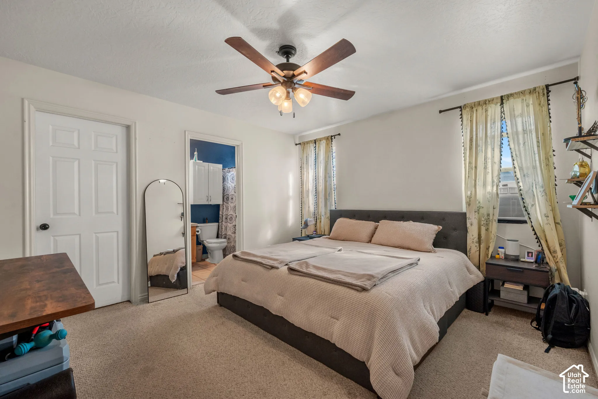 Carpeted bedroom featuring a ceiling fan with integrated lighting, a paneled door, and an entryway to a bathroom